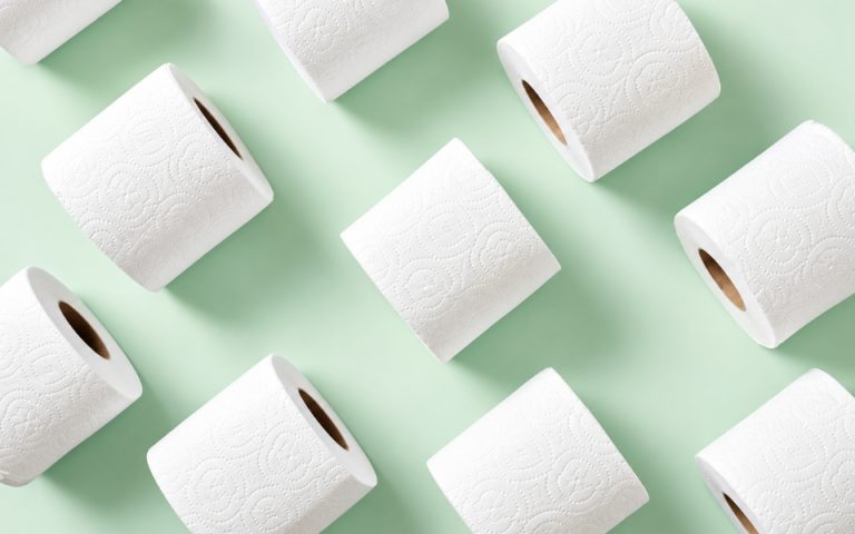 Valkoisia wc-paperirullia vaaleanvihreällä taustalla